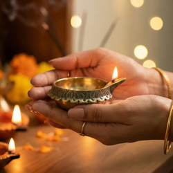 Hand holding a lit oil lamp with blurred lights in the background